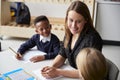 Elevated view of a female primary school teacher sitting between two school kids at table in a classroom, smiling at each other du Royalty Free Stock Photo