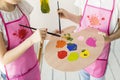 elevated view two girls same pink apron mixing paint wooden palette with paint brush. High quality photo