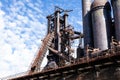 Elevated walkway alongside steel mill blast furnaces against a blue sky with clouds