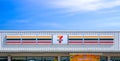 7-Eleven logo signboard on white corrugated metal roof of modern convenience store against blue sky background