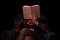 Woman with open book on armchair. Shot from front, evening time