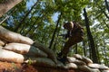 An elite soldier adeptly clears military barriers in the perilous wooded terrain, showcasing tactical skill and agility