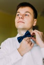 Ellegant handsome groom buttoning his bow tie in a hotel room
