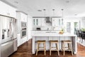 A large, luxurious white kitchen with bar stools under the island.