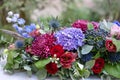 Elongated floral arrangement in vintage metal vase. table setting. Blue and red color. Gorgeous bouquet of different Royalty Free Stock Photo