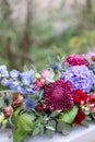 Elongated floral arrangement in vintage metal vase. table setting. Blue and red color. Gorgeous bouquet of different