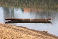 Elongated old dilapidated light brown wooden river boat made from wooden boards left tied with rusted chain Royalty Free Stock Photo