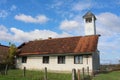 Elongated small old local catholic church with white bell tower covered with metal roof and shiny new cross on top Royalty Free Stock Photo