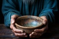 Emaciated hands hold an empty bowl against wood, depicting the reality of hunger