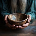 Emaciated hands hold an empty bowl against wood, depicting the reality of hunger