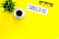 Email subscribe concept. Hand lettering subcribe on work desk with plant, glasses, cup of coffee on yellow background