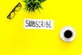Email subscribe concept. Hand lettering subcribe on work desk with plant, glasses, cup of coffee on yellow background