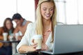 Emails over a cup of coffee. A beautiful young woman using her laptop in a busy coffee shop. Royalty Free Stock Photo