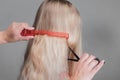 Emale hairdresser hold in hand between fingers lock of blonde hair, comb and scissors closeup. Image of hairdresser trimming ends