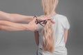 Emale hairdresser hold in hand between fingers lock of blonde hair, comb and scissors closeup. Image of hairdresser trimming ends