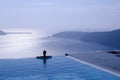 Female silhouette in infinity pool on cliff, Santorini, Greece