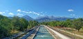 Embankment of the Bolshaya Almatinka River, along which people walk. Mountains of the Trans-Ili Alatau in the distance.