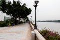 Embankment with flowers on the railing. Stone path along the river. Big green trees, black lights.