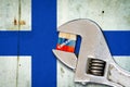 Embargo. Word on a wooden block in the colors of the Russian flag. Clamped wrench. Against the background of the flag of Finland.
