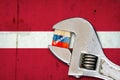 Embargo. Word on a wooden block in the colors of the Russian flag. Clamped wrench. Against the background of the flag of Latvia.