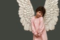 An embarrassed angel on a gray asparagus background.  Cute little girl in pink dress with angel wings. Copy space Royalty Free Stock Photo