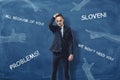 Embarrassed businessman standing near dark blue wall with hands pointing to him and blaming words drawn on it. Royalty Free Stock Photo