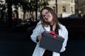 Embarrassed happy young girl with gift in her hands smiles. Young woman is neatly holding black box with red bow