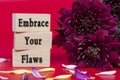 Embrace your flaws text on wooden cube and with flowers bouquet background.