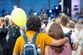 Embracing young people standing in the crowd and watching an open-air concert. View from the back.