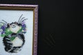 Embroidered striped grey fat cat with a bouquet of violet flowers on a white canvas. Metal embroidery needles. Royalty Free Stock Photo