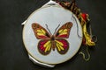 Embroidered  bright butterfly on white cotton fabric stretched on a wooden Hoop with colored threads and scissors lying on black p Royalty Free Stock Photo