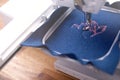 Embroidery area of a sewing machine where boiled wool in classic blue color is being equipped with a pink magnolia embroidery