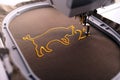 Embroidery hoop and needle foot of an embroidery machine stitching ox symbol and number 21 with golden yarn on shiny fabric