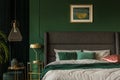 Emerald green and golden poster above comfortable king size bed with headboard and pillows in dark green bedroom