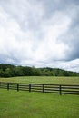 Emerald green meadow with horizon tree line, black rail fence and turbulent clouds, creative copy space