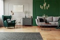 Green wing back chair with pillow in grey living room interior with wooden commode