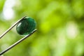 Emerald. Natural stone without processing in tweezers on a green background. Place for text