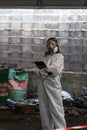 emergency pollution factory concept. Female chemist wearing PPE and gas mask inspecting oil on factory floor