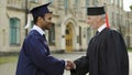 Eminent professor giving diploma to male student shaking hand convocation day