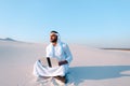 Emirati guy professional designer with computer projects project, sitting on sand in desert on summer evening. Royalty Free Stock Photo