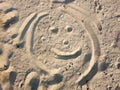 Emoticon painted on the sand. Funny physiognomy, face. Smile on the beach.