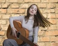 Emotion concept. Portrait of a young girl playing the guitar in front of the brick wall background Royalty Free Stock Photo