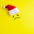 Emotion of sad face expression and red santa claus hat on yellow background. Concept of a miserable new year and christmas. Copy Royalty Free Stock Photo