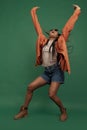 Emotional african girl in shorts and shirt dancing, having fun isolated on dark green background. Concept of beauty, art Royalty Free Stock Photo