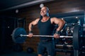 Emotional aged bald bodybuilder doing trapezius and deltoid exercise with a barbell in the gym Royalty Free Stock Photo