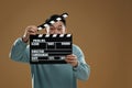 Emotional asian actor with clapperboard on brown background, space for text. Film industry