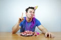 Emotional beautiful caucasian man with birthday party cone hat on head and crumple cake raises your index finger up. People and li Royalty Free Stock Photo