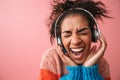 Emotional beautiful young african woman posing  over pink wall background listening music with headphones Royalty Free Stock Photo