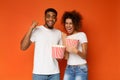 Emotional black couple enjoying movie with buckets of popcorn