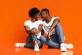 Emotional black lovers cuddling on orange background